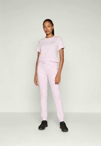 T-shirt in cotone rosa e pantaloni della tuta abbinati, entrambi con una vestibilità comoda. La T-shirt ha maniche corte e un piccolo logo ricamato. Sneakers nere.