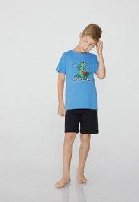 Blaues Baumwoll-T-Shirt mit einem Dinosaurier-Motiv mit einer Gitarre und Text, kombiniert mit schwarzen Shorts. Auf einem hellen Hintergrund präsentiert.