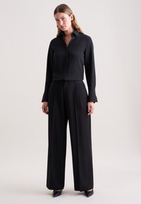 Zwarte langemouwen shirt met een button-down kraag, gecombineerd met hoge taille zwarte wijde broek. Gladde stof, minimalistisch ontwerp.