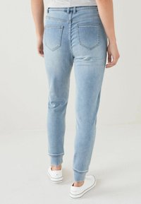 Pantalones jogger de mezclilla azul claro con pierna ajustada, que cuentan con dos bolsillos traseros y puños acanalados. Combinados con zapatillas blancas.