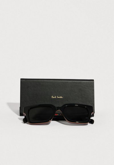 Fekete téglalap alakú napszemüveg sötét lencsékkel, színes díszítésekkel az oldalán, fekete bőr tokban, amelyen a "Paul Smith" felirat látható.