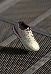 Cream-colored sneaker with maroon accents, smooth synthetic upper, padded collar, and a textured sole. Features lace closure and brand logo.