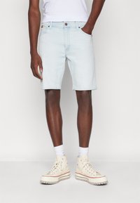 Pantalones cortos de mezclilla azul claro con corte recto, bolsillos y dobladillos enrollados, combinados con zapatillas deportivas blancas de caña alta y calcetines blancos de caña corta.