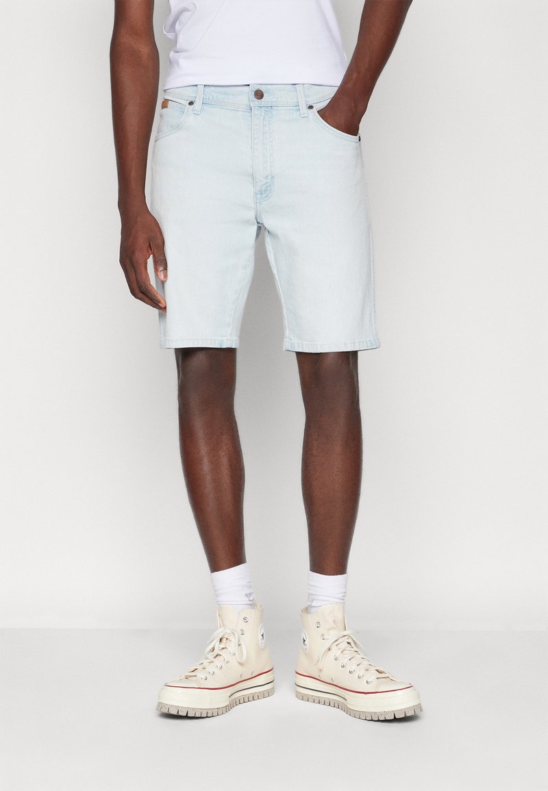 Pantalones cortos de mezclilla azul claro con corte recto, bolsillos y dobladillos enrollados, combinados con zapatillas deportivas blancas de caña alta y calcetines blancos de caña corta.