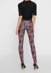 Leggings med ett svart elastiskt midjeband, med ett färgglatt blommönster i rött, blått och svart på en vit bakgrund.