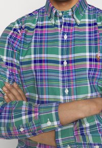 Green and blue plaid shirt featuring varying stripes of pink and white. Button-up style with a classic collar and button cuffs.