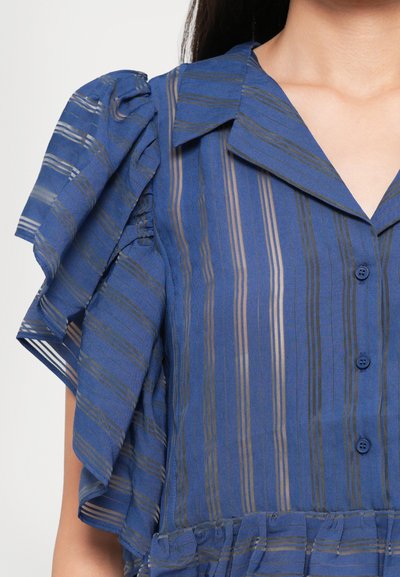 Woman wearing a blue button-front blouse with vertical stripes and ruffled short sleeves featuring a collar and gathered waist detail.