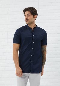 Navy short-sleeve shirt with a banded collar, front pocket, and white buttons. Fabric appears smooth with a slight sheen.