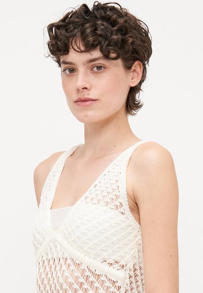 Haut en tricot léger de couleur crème avec un motif géométrique, présentant un décolleté en V et des bretelles larges. Texture douce avec un design superposé.