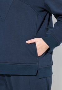 Sweatshirt blu navy caratterizzato da un tessuto texturizzato, polsini a coste e una tasca a marsupio sul davanti, con dettagli delle cuciture che aggiungono dimensione.