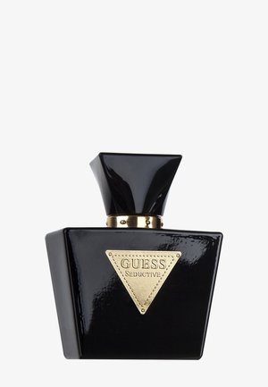 Zwart rechthoekig parfumflesje van Guess Seductive met een grote geometrische zwarte dop en een gouden driehoekig etiket aan de voorkant.