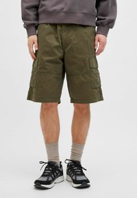 Shorts cargo vert olive avec plusieurs poches à rabat, en tissu durable. À porter avec des chaussures de sport grises et des chaussettes crew beiges.