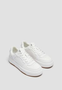 Ein Paar weiße Sneaker mit niedrigem Schnitt, gelochten Zehenkappen, Schnürsenkeln, gepolsterten Schuhkragen und braunen Gummisohlen auf einem hellgrauen Hintergrund.