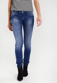 Slim-fit blå jeans med slitna detaljer, femfickorsdesign, lätt blekning, kombinerat med en svart och vit randig topp och svarta ankelstövlar.