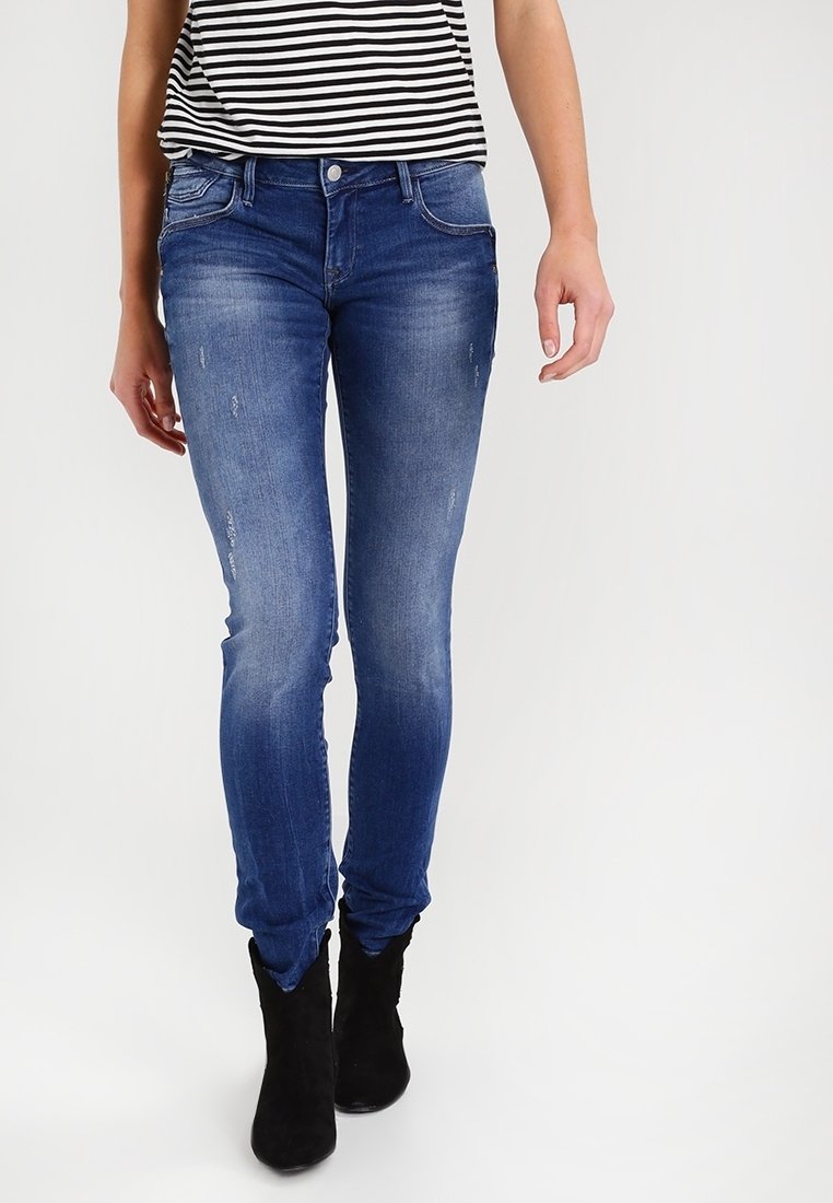 Slim-fit blå jeans med slitna detaljer, femfickorsdesign, lätt blekning, kombinerat med en svart och vit randig topp och svarta ankelstövlar.