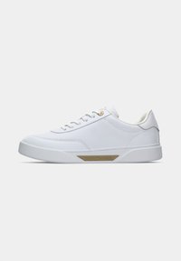 Sneaker alb cu vârful jos, cu închidere prin șireturi, eyelet-uri aurii și logo-ul Tommy Hilfiger pe partea laterală a tălpii, pe un fundal simplu de culoare deschisă.