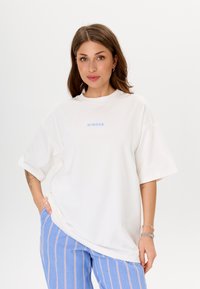 Witte oversized T-shirt met nabijgelegen blauwe geborduurde tekst, gecombineerd met lichtblauwe gestreepte broek. Gladde katoenstof en een comfortabele pasvorm.