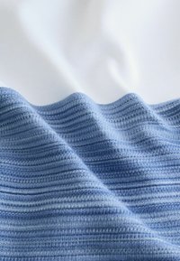 Tissu textile présentant un design ondulé en bleu et blanc. Texture douce avec des rayures horizontales dans des nuances variées de bleu.