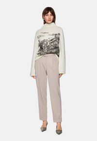 Knit sweater with beige and gray architectural print, paired with light taupe trousers. Model wears pointed toe heels and large earrings.