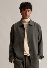 Szary żakiet zapinany na guziki z wyraźnym kołnierzem, noszony na dopasowanym kremowym golfie. Gładka tekstura i luźny krój.