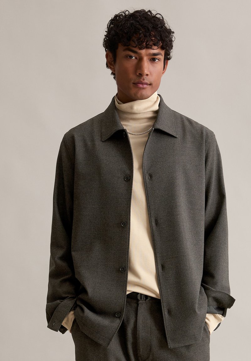 Szary żakiet zapinany na guziki z wyraźnym kołnierzem, noszony na dopasowanym kremowym golfie. Gładka tekstura i luźny krój.