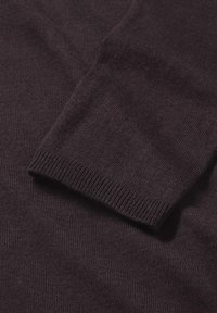 Manica di un maglione lavorato a maglia di colore viola scuro con polsini a coste, texture liscia e un leggero lucido, che evidenzia un design classico e aderente.