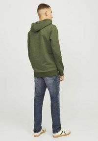 Sudadera verde oscura con un diseño en la costura trasera, puños y dobladillo de canalé. Combinada con jeans azules y zapatillas blancas con rayas verdes.