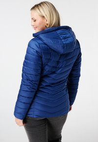 Blauwe pufferjack met een chevronpatroon, capuchon en ribbelkraag. Gemaakt van glanzend, soepel materiaal, met een getailleerde pasvorm en lange mouwen.