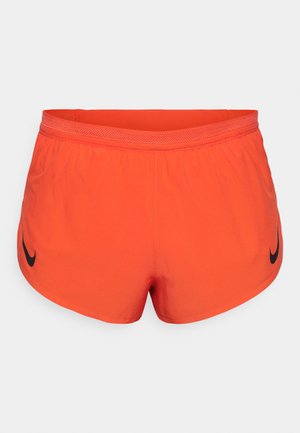 Oranžid sportlikud lühikesed püksid, mis on valmistatud siledast kangast, vasakul küljel on must Nike'i logo ning mugavuse tagamiseks elastne vöö. 