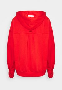 Sudadera roja con capucha, con un escote redondo, puños acanalados y un dobladillo fruncido. En la parte posterior aparece "J.D.L." en letras pequeñas.