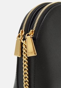 Svart läderväska med strukturerad yta, guldfärgade dragkedjor och kedjedetaljer. Har varumärkesetikett på metallkomponenter. Rund form med elegant design.