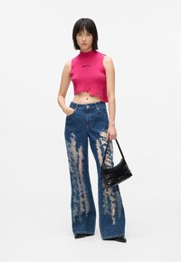 Rozā cropped adīta blūze ar augstu kaklu un neapstrādātu apakšmalu, kopā ar nolietotām zilām platu kāju džinsiem ar lieliem iegriezumiem. Iekļauta melna rokassoma.