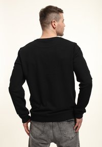 Sweatshirt noir à manches longues, avec des poignets côtelés et un col rond. Le tissu semble lisse, avec une couleur unie et uniforme. Vue de dos.