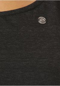 Mustat, tekstuurilliset kankaat, joissa on pyöreä kaula-aukko; siinä on ympyrän muotoinen hopeinen logo, jossa lukee "since 1993" ja sydämen muoto.