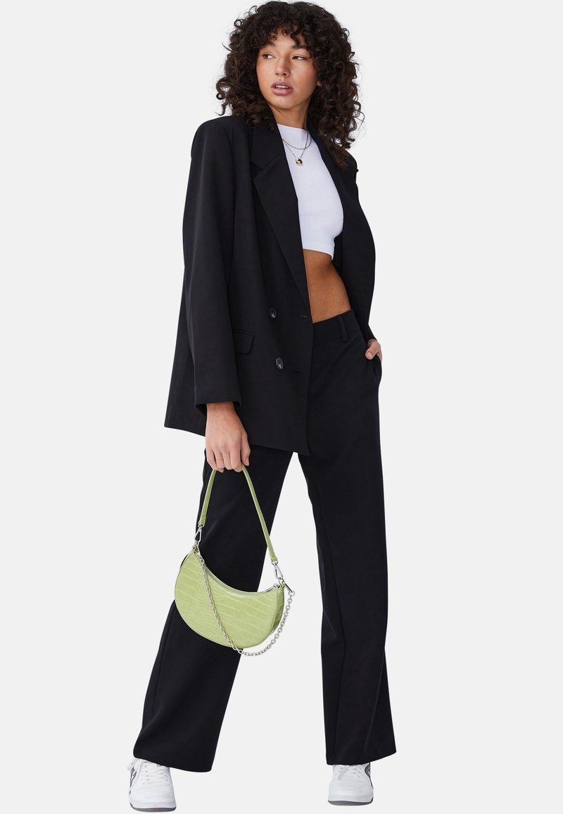 Czarna, dopasowana marynarka i spodnie, biała krótka bluzka, zielona torebka imitująca krokodyla z łańcuchem oraz białe sneakersy, tworzą nowoczesną stylizację.