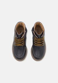 Bottines en cuir de marine avec doublure intérieure en tan, lacets jaunes et fermetures éclair sur le côté. Elles présentent une forme arrondie et des coutures blanches contrastantes.