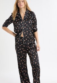 Czarny zestaw piżamowy w kwiaty, składający się z zapinanego na guziki topu z białą lamówką i długimi rękawami oraz luźnych spodni w drobne różowe kwiatki.