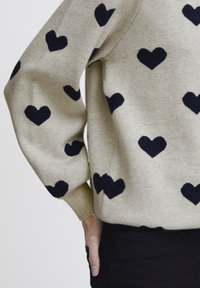 Maglione beige con motivi a forma di cuore blu navy, polsini a coste e una vestibilità rilassata. Tessuto morbido con un design casual.