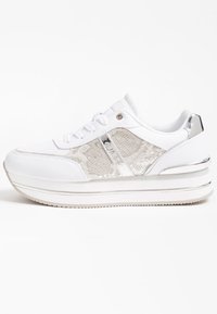 Bílé tenisky s lesklým stříbrným akcentem, texturovanými stranami a vrstvenou platformovou podrážkou. Mají šňůrky a jemné detaily značky.