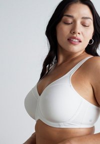 White bra with molded cups, smooth fabric, adjustable straps, and subtle stitching details. Includes branding on the side.