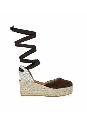 Alpargata de cuña con puntera de ante marrón, contrafuerte tejido blanco, plataforma de cuerda trenzada y largos lazos negros para atar alrededor del tobillo.