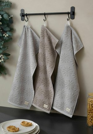 Drei hängende Küchentücher mit Schneeflockenmuster in Grau und Beige an einem schwarzen Wandhalter, nahe bei Tellern mit Keksen und einem Glas mit Brezeln.