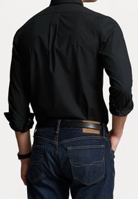 Svart knappad skjorta med uppvuxna ärmar, figursydd design, kombinerad med mörkblå jeans som har en läderlapp och kontrasterande sömmar på fickorna.