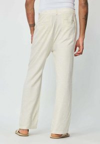 Pantalons en lin beige clair avec un design à jambe droite, comprenant deux poches arrière et une texture lisse. Coupe décontractée, idéale pour les temps chauds.