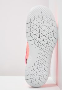 Semelle d'une chaussure de sport rose avec une semelle blanche présentant des rainures triangulaires et en forme de diamant pour l'adhérence.