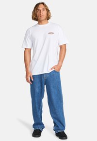 Hvid bomulds t-shirt med et lille mønstret logo på brystet, parret med løse blå denim jeans og sorte sko.