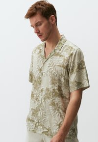Korte mouw knoopshirt in lichtbeige met een groen tropisch bloemenpatroon, gemaakt van een soepel stof, met een losse kraag en knopen aan de voorkant.
