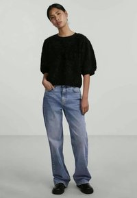 Black fuzzy short-sleeve sweater, high-waisted light blue jeans, and black shoes. The outfit combines soft texture and casual fit.