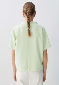 Top corto a maniche corte verde chiaro realizzato in un tessuto testurizzato. Presenta una vestibilità comoda, un colletto basso e un orlo dritto sul retro.