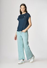 Top blu navy a maniche corte con vestibilità ampia, abbinato a jeans a gamba larga blu chiaro e sneakers bianche. Dettaglio logo discreto sul top.